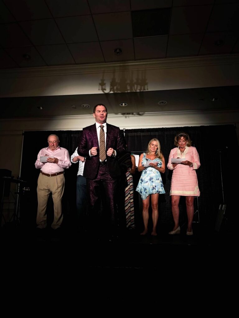 Michael performing on stage at a country club event. There are volunteers on stage behind him.