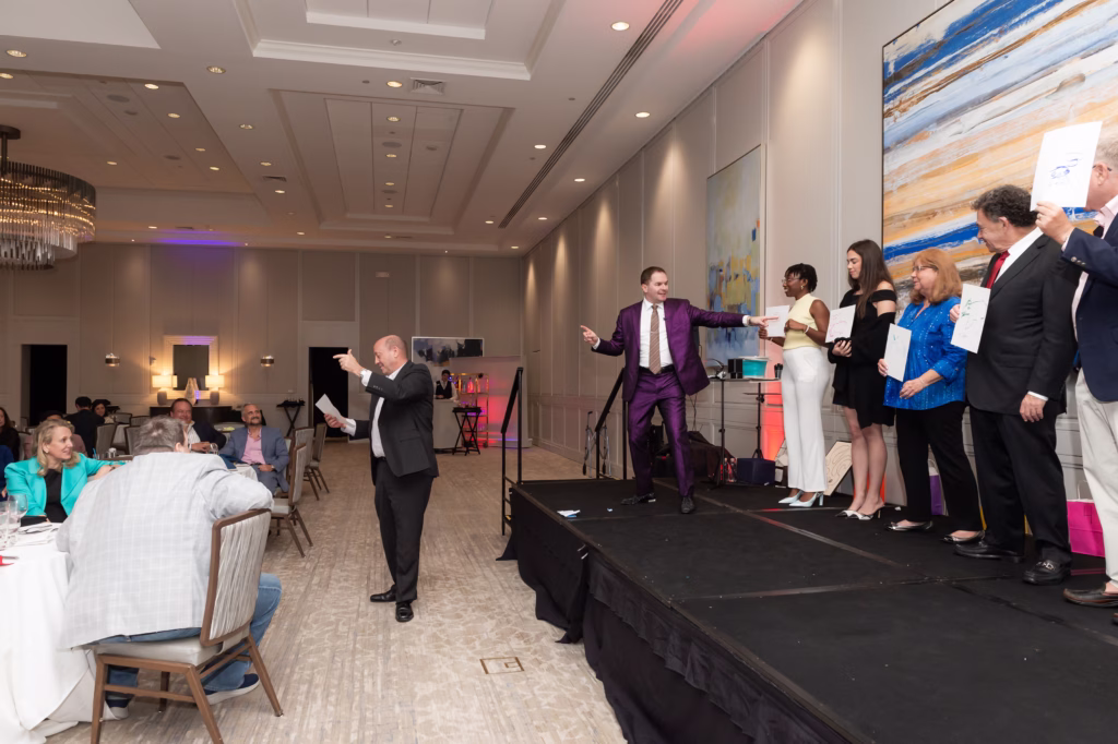 Michael, on stage in a purple suit, with 5 volunteers holding signs up in a ballroom