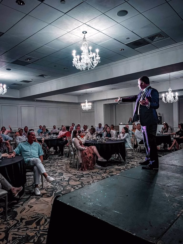 Michael Gutenplan on a stage as Emcee at an event at a country club.