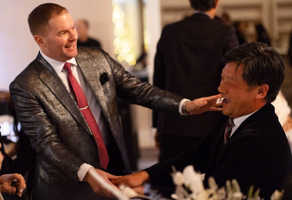 Michael performing a card trick for a laughing guest at an event.