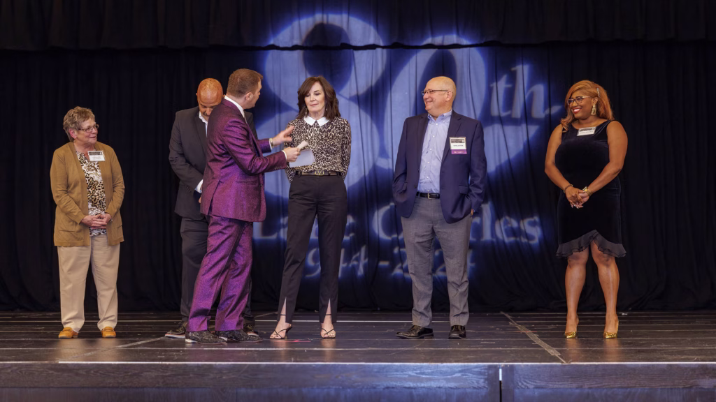 Michael on a stage at a corporate event. Five people stand with him, smiling and having fun.