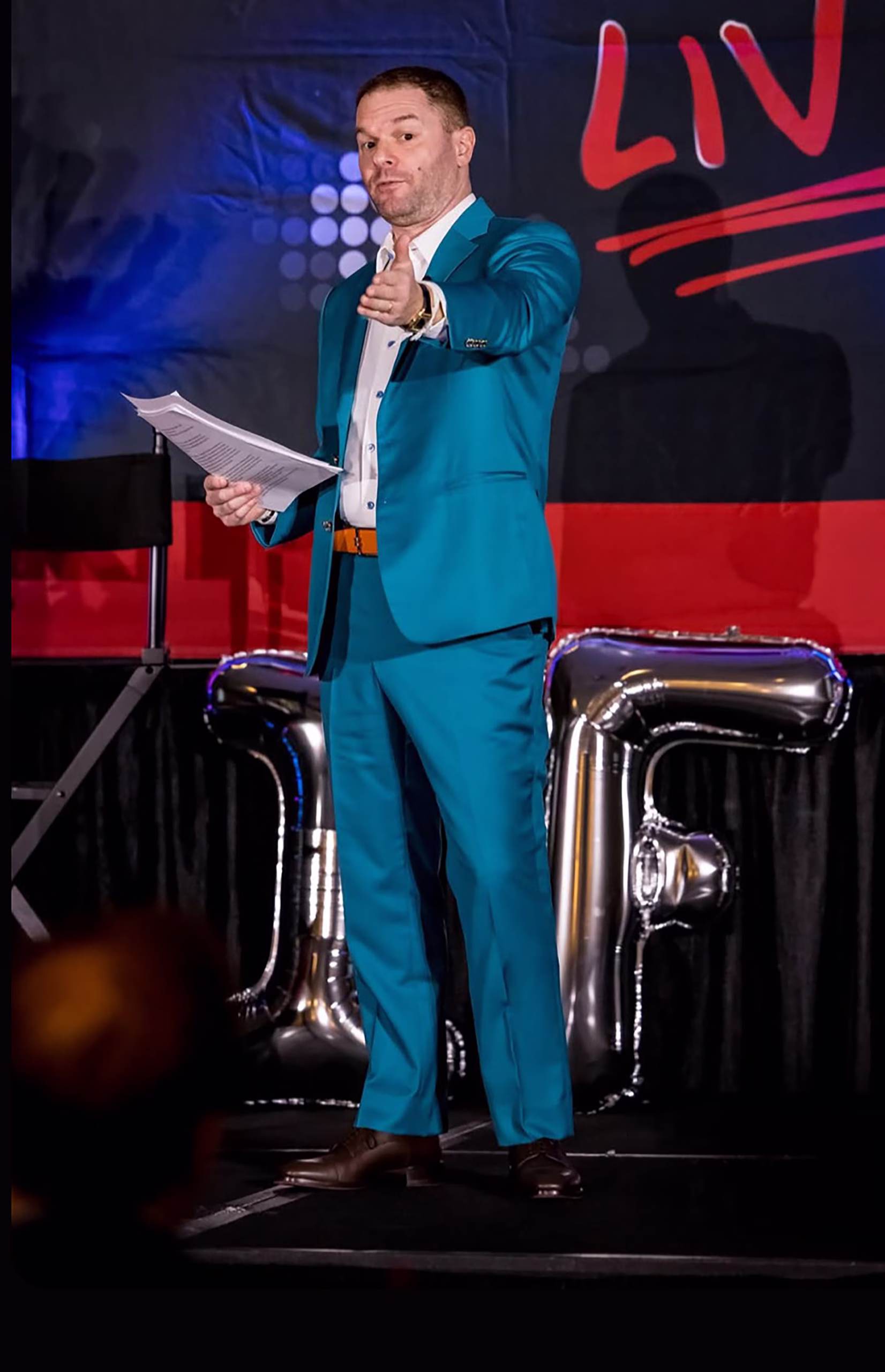 Michael, on stage as an auctioneer at an association conference, in a teal suit.